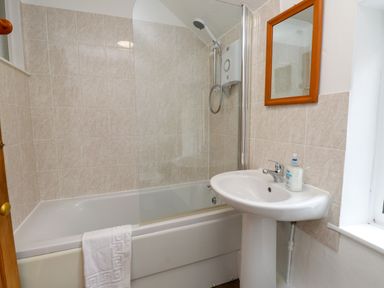 A bathroom with a bathtub shower combination a white sink with soap and a mirror above at Nantmel in Beddgelert