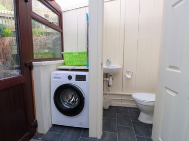 A small utility room with a washing machine a green laundry basket a sink and a toilet at Nantmel in Beddgelert