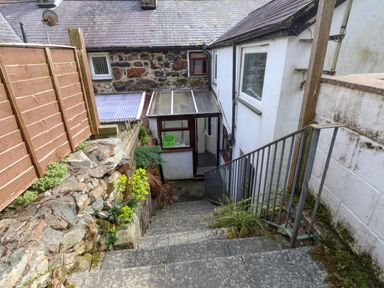 A stone staircase with a metal railing leading down to a small covered entrance of a building with a stone wall and wooden fence at Nantmel in Beddgelert