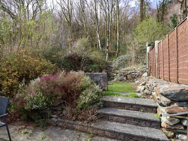 An outdoor garden area with stone steps leading up to a grassy section and trees at Nantmel in Beddgelert