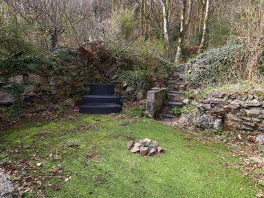 A small outdoor seating area with two black chairs on green grass surrounded by stone walls and trees at Nantmel in Beddgelert