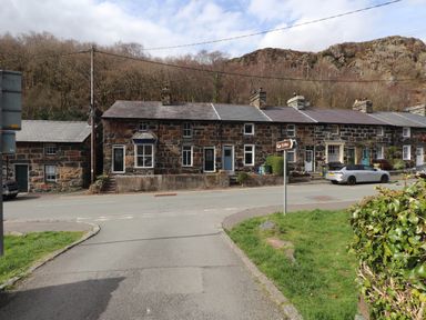 A row of stone cottages along a road with a car parked and a signpost pointing to Ty Afon at Nantmel in Beddgelert