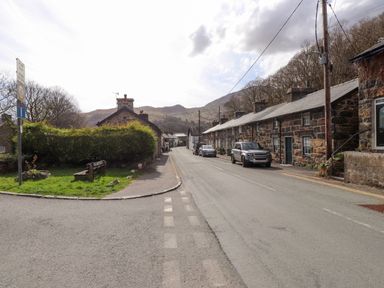 A narrow street with stone houses parked cars and green bushes with hills in the background at Nantmel in Beddgelert