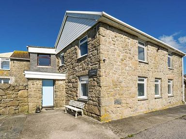 A stone house with multiple windows and a white bench outside at Tregiffian Vean in Sennen Cove