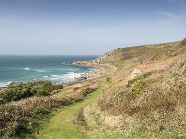 A coastal path with grassy hills and rocky shoreline by the sea at Tregiffian Vean in Sennen Cove