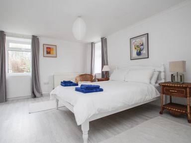 A bedroom with a white bed and blue towels on it two bedside tables with lamps two windows with gray curtains and two paintings on the walls at Tregiffian Vean in Sennen Cove