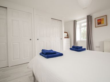A bedroom with a white bed and blue towels folded on top next to a window with gray curtains at Tregiffian Vean in Sennen Cove