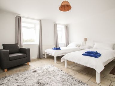 A bedroom with two single beds with blue towels a gray armchair and a rug at Tregiffian Vean in Sennen Cove