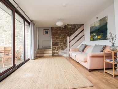 A living room with a sofa cushions a side table and a large rug next to a sliding glass door at Tregiffian Vean in Sennen Cove