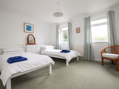 A bedroom with two single beds a chest of drawers with a mirror two windows with curtains and a chair at Tregiffian Vean in Sennen Cove