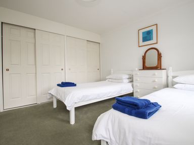 A bedroom with two single beds with blue towels a white dresser with a mirror and sliding closet doors at Tregiffian Vean in Sennen Cove