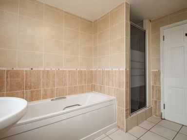 A bathroom with a bathtub a shower with glass door a white sink and a white door at Tregiffian Vean in Sennen Cove