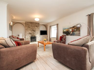 A living room with sofas a coffee table and a stone fireplace at Tregiffian Vean in Sennen Cove