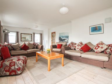 A living room with sofas a wooden coffee table a rug and framed pictures on the walls at Tregiffian Vean in Sennen Cove