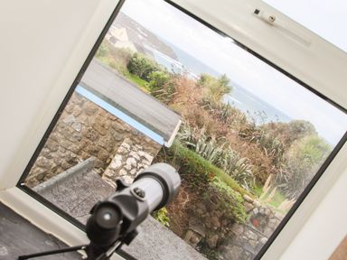 A telescope on a windowsill overlooking a stone wall garden and the sea at Tregiffian Vean in Sennen Cove