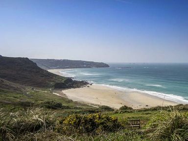 A coastal view with a sandy beach and ocean waves near cliffs and grassy hills at The Coach House in Sennen near St Just