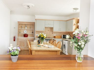 A kitchen and dining area with wooden table and chairs and flowers on the table and counter at The Coach House in Sennen near St Just