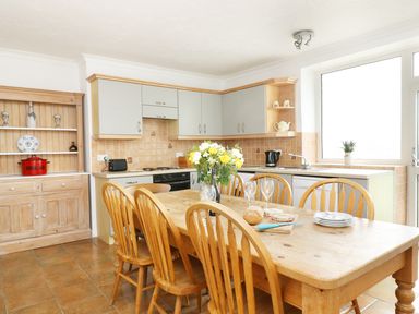 A kitchen with a wooden dining table and chairs with flowers and dishes on the table at The Coach House in Sennen near St Just