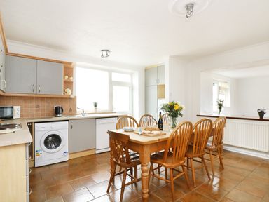 A kitchen with wooden table and six chairs a washing machine dishwasher and microwave at The Coach House in Sennen near St Just