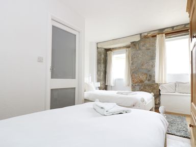 A bedroom with two single beds a wooden wardrobe stone walls and windows with curtains at The Coach House in Sennen near St Just