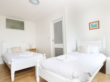 A bedroom with two single white beds, a nightstand with a lamp, and a small framed picture on the wall at The Coach House in Sennen near St Just