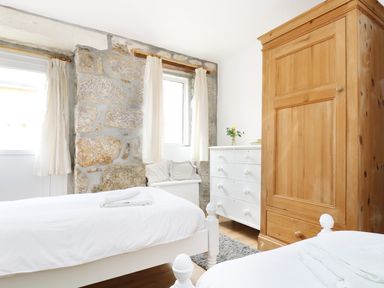 A bedroom with two single beds a wooden wardrobe a white chest of drawers and stone walls at The Coach House in Sennen near St Just