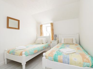 A bedroom with two single beds a nightstand with lamp and a window with curtains at The Coach House in Sennen near St Just