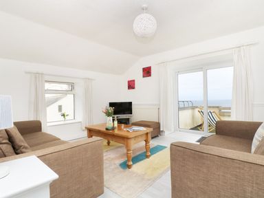 A living room with brown sofas a wooden coffee table a rug and a balcony with deck chairs at The Coach House in Sennen near St Just