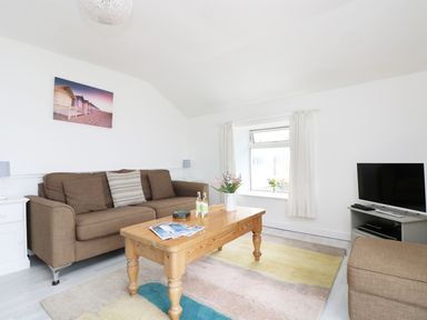 A living room with a brown sofa wooden coffee table and television at The Coach House Sennen near St Just