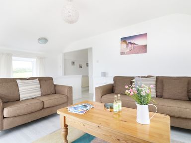 A living room with two brown sofas a wooden coffee table and a white pitcher with flowers at The Coach House in Sennen near St Just