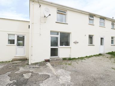 The exterior of a white house with several windows and doors a satellite dish and a gravel driveway at The Coach House in Sennen near St Just