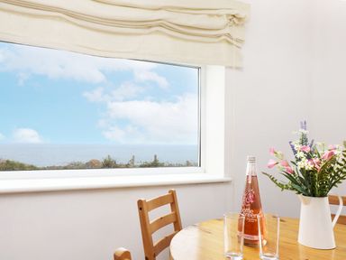 A dining room with a table, chairs, flowers, and a bottle of beverage at The Coach House in Sennen near St Just