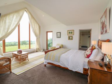 A bedroom with a wooden bed a chair a coffee table beside large windows at Millers Lane House Muff County Donegal