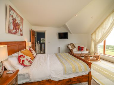 A bedroom with a wooden bed and floral pillows a sofa with cushions a coffee table and large window at Millers Lane House in Muff County Donegal
