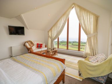 A bedroom with a wooden bed a wicker loveseat a glass coffee table and a large window with curtains at Millers Lane House in Muff County Donegal