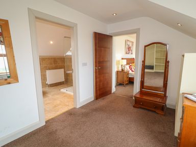 A room with a wooden framed mirror, a wooden chest of drawers, a doorway leading to a bathroom with tiled walls and a brown wooden door opening to a bedroom at Millers Lane House in Muff County Donegal