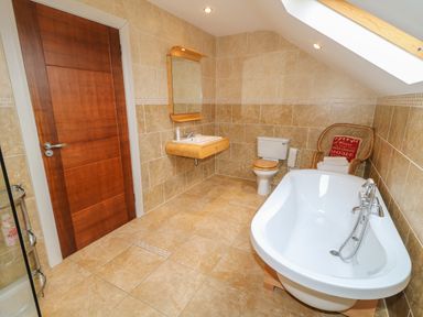 A bathroom with a wooden door a wall-mounted sink a toilet a freestanding bathtub and a wicker chair with towels at Millers Lane House in Muff County Donegal