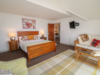 A bedroom with a wooden bed and nightstands lamps a couch a glass coffee table and a wall mounted tv at Millers Lane House in Muff County Donegal