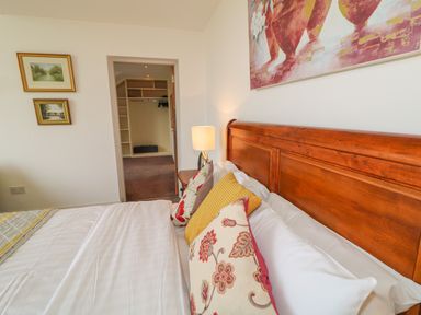 A bedroom with a wooden bed, patterned pillows, a lamp on a nightstand, and an open door leading to a walk-in closet at Millers Lane House in Muff County Donegal