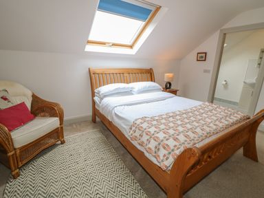 A bedroom with a wooden bed wicker chair next to a skylight window at Millers Lane House in Muff County Donegal