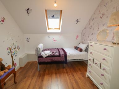 A bedroom with a single bed under a skylight window a white dresser with a lamp and mirror fairy wall decals and a wooden floor at Millers Lane House in Muff County Donegal