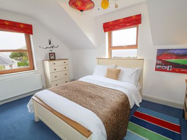 A bedroom with a bed chest of drawers two windows and Manchester United decor at Millers Lane House in Muff County Donegal