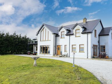 A large white two-story house with multiple windows and a front door surrounded by a green lawn and gravel driveway at Millers Lane House in Muff County Donegal