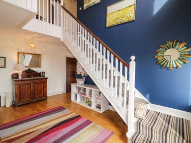 A staircase with striped carpet and blue wall with artwork and mirror in a hallway with wooden floor and a striped rug at Millers Lane House Muff County Donegal