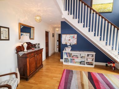 An entryway with wooden flooring a white staircase blue wall a wooden cabinet with a lamp and a white shelf with books at Millers Lane House Muff County Donegal