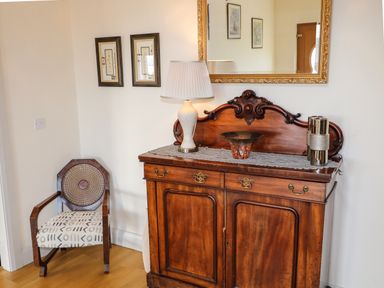 A wooden sideboard with decorative items and a chair in a corner at Millers Lane House in Muff County Donegal