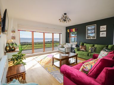 A living room with large windows showing a landscape with sofas a wooden coffee table and plants at Millers Lane House in Muff County Donegal