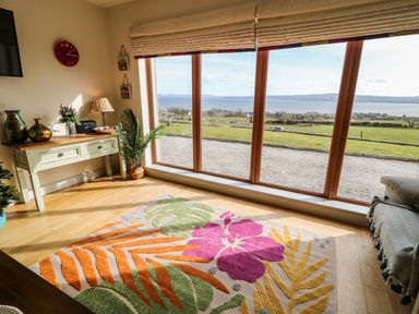 A room with a floral rug and large windows overlooking a grassy area and water at Millers Lane House in Muff County Donegal