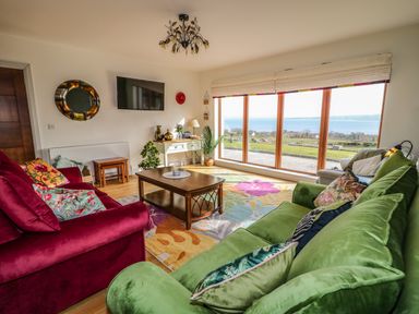 A living room with green and red sofas a wooden coffee table a colorful rug and large windows overlooking a grassy landscape at Millers Lane House in Muff County Donegal