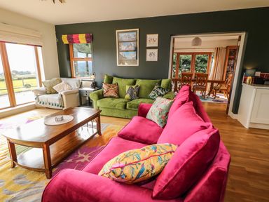 A living room with pink and green sofas wooden coffee table and dining area visible through doorway at Millers Lane House in Muff County Donegal